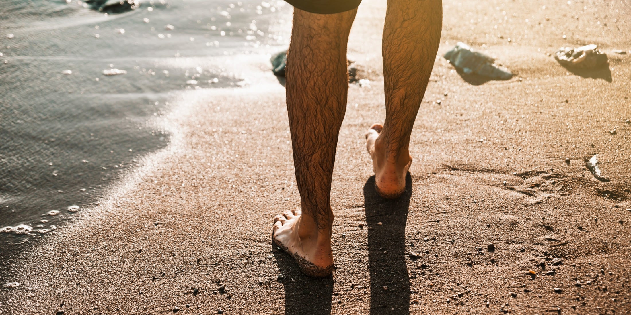 A man walking barefoot along the beach, showcasing the importance of foot care and allowing feet to breathe as part of overall hygiene tips for men. The image emphasizes maintaining clean, healthy feet and the benefits of fresh air and natural surfaces for foot hygiene.