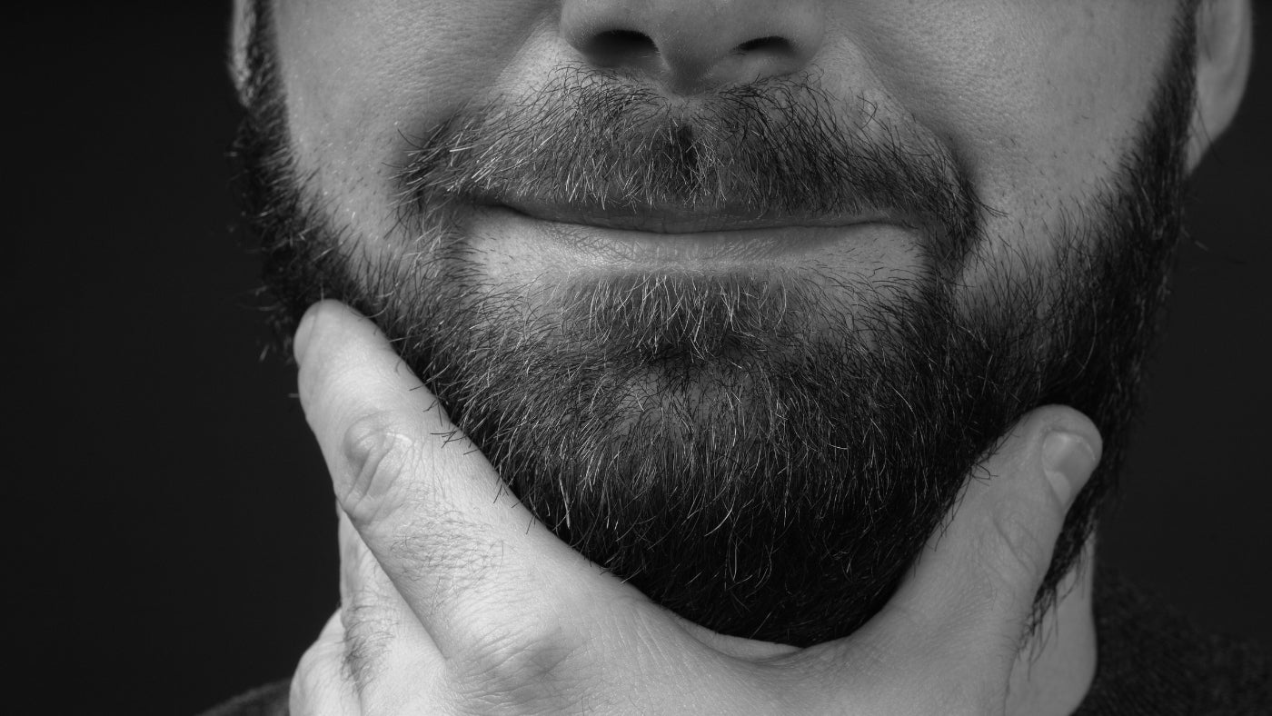 Smiling man in black and white photo thoughtfully touching his chin with a well-groomed 3 month beard