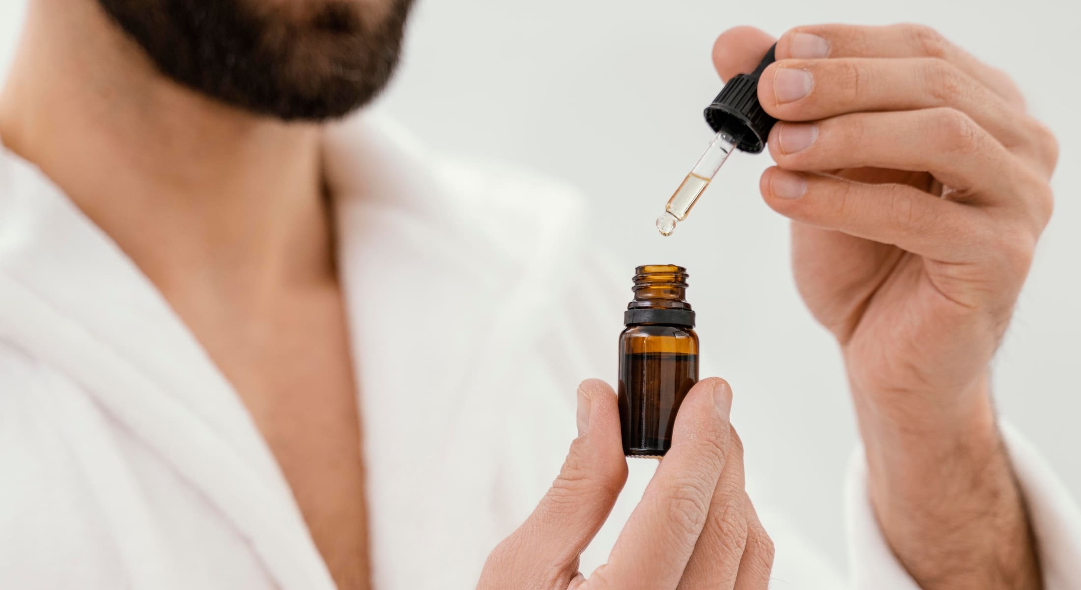 Close-up of a man holding a dropper and bottle of beard oil, emphasizing the importance of using beard oil for maintaining a well-groomed and healthy beard.