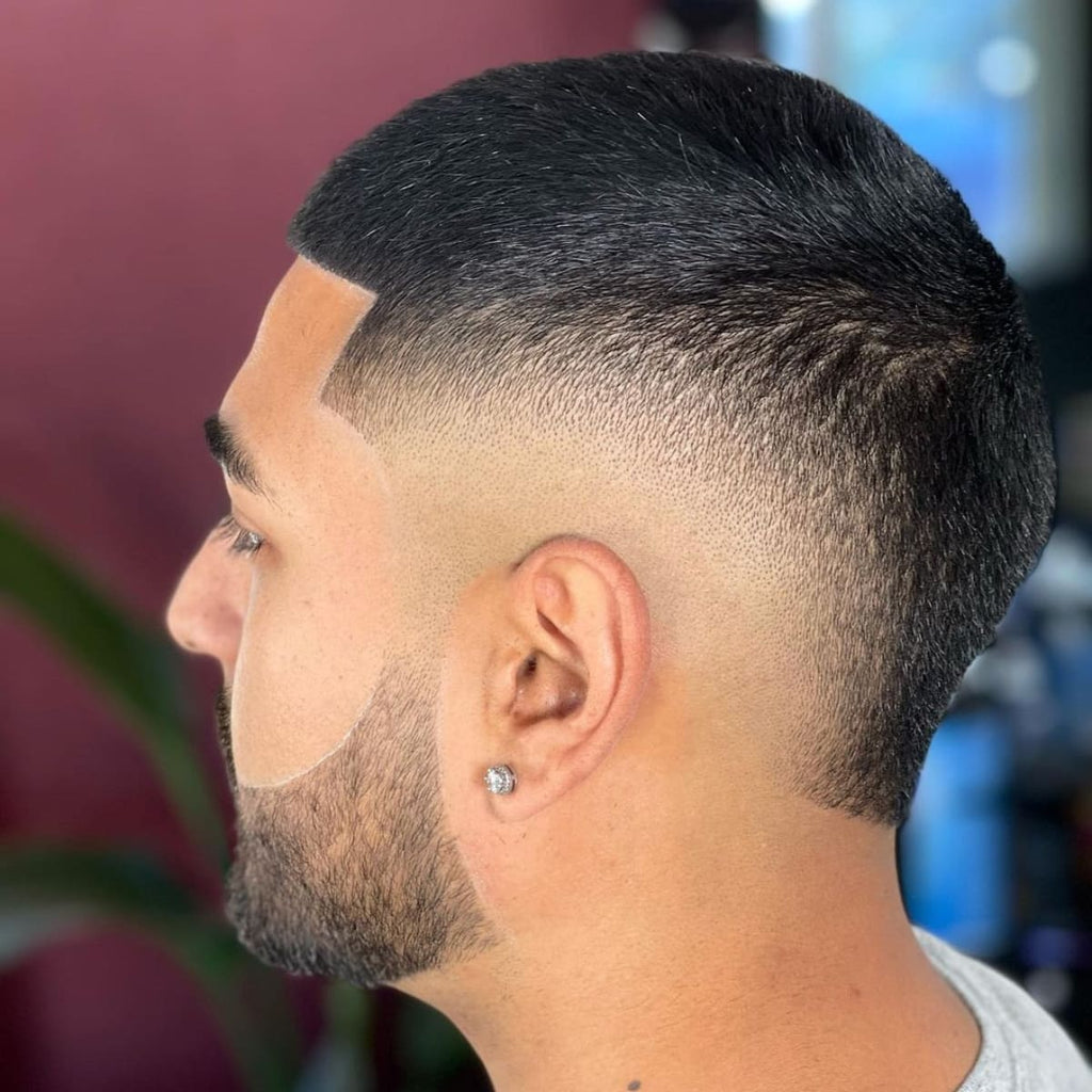 Side profile of a man showcasing a sharp buzz cut burst fade. The clean, tapered fade blends smoothly around the ears, while the well-groomed beard adds to the polished look, creating a sleek and modern hairstyle.