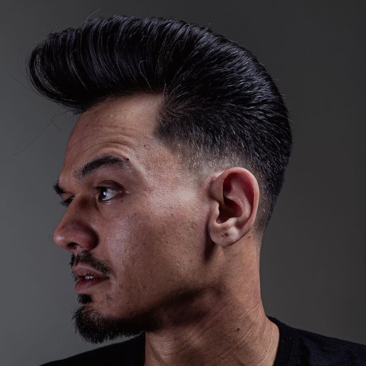 Side profile of a man sporting a classic low fade pompadour, featuring a high, voluminous top and sharply faded sides for a bold, structured look.