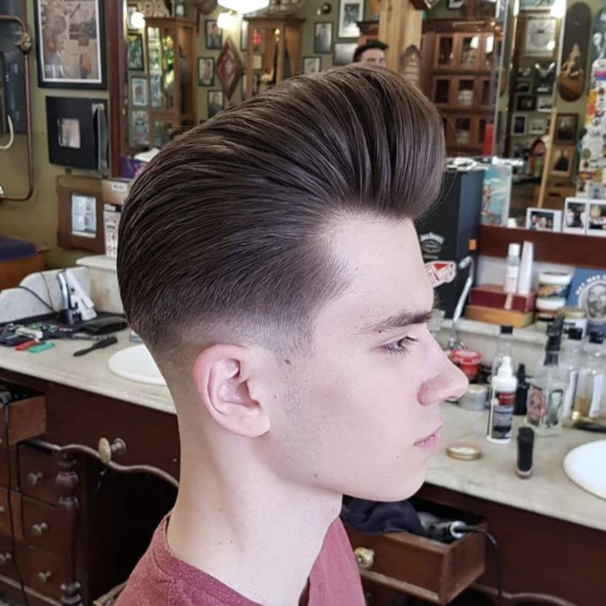 Side view of a man with a high-volume hairstyle, featuring a sleek, lifted top and smoothly faded sides, captured in a classic barbershop setting.