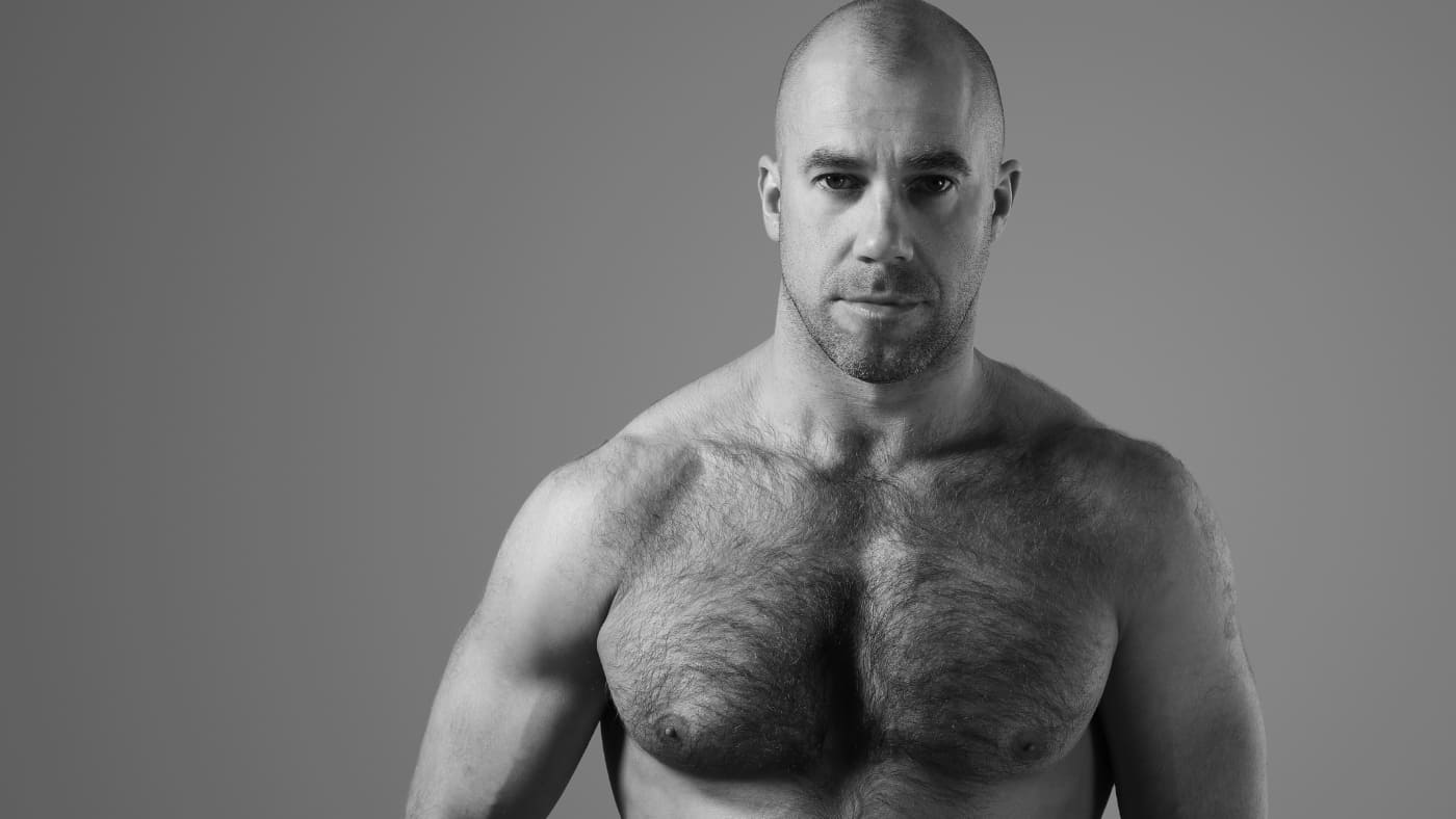 Muscular bald man with chest hair posing in a black and white portrait