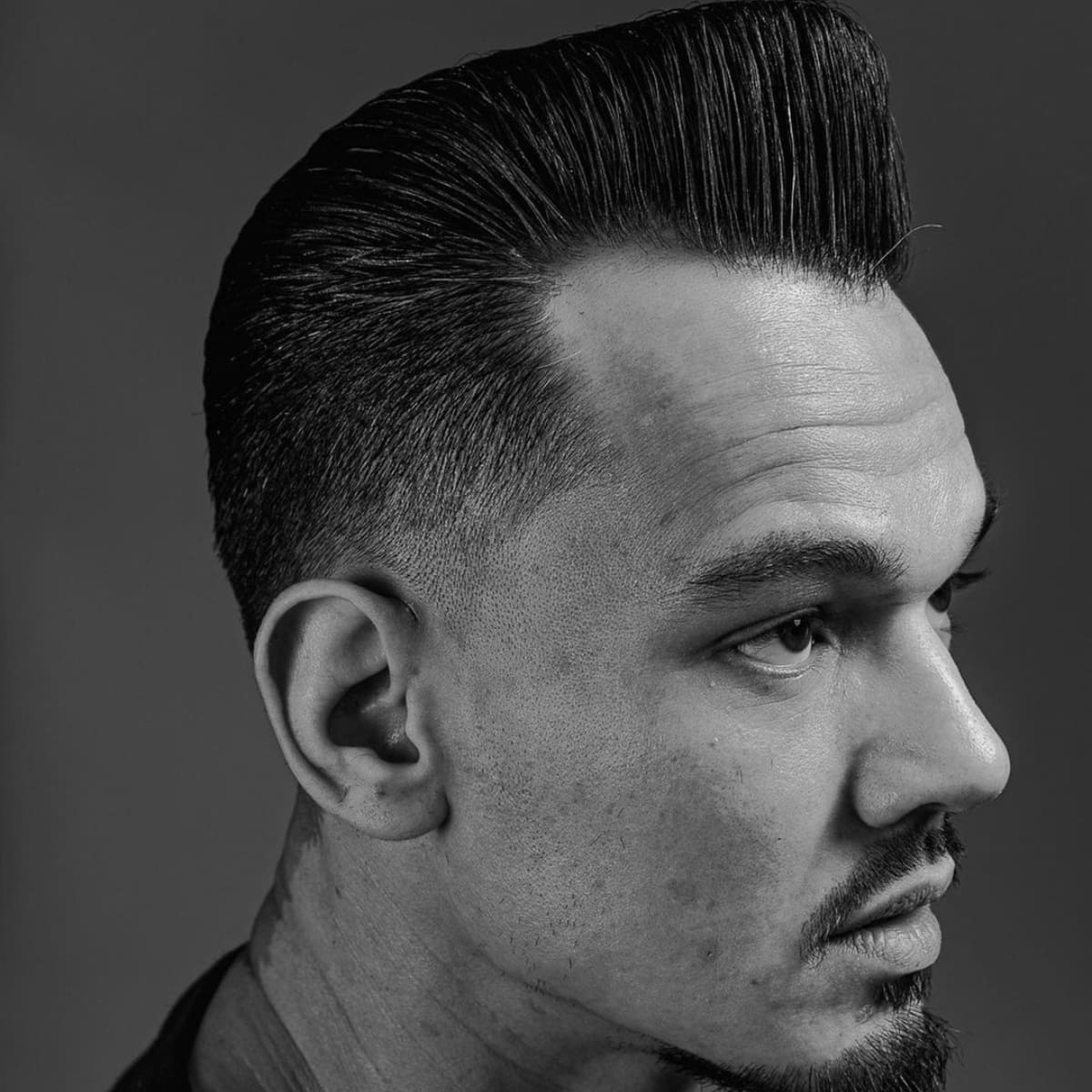 Black and white profile of a man with a short, voluminous low fade pompadour, featuring a sleek top and tight faded sides for a sharp, classic look.