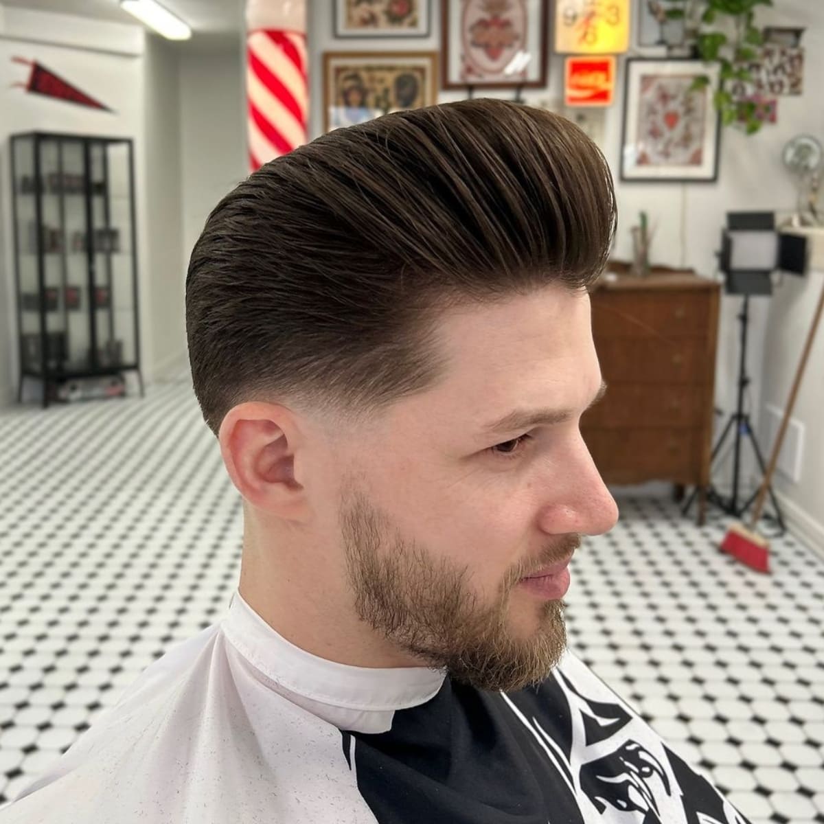 Man with a textured low fade pompadour hairstyle, featuring a voluminous top and neatly faded sides, paired with a trimmed beard for a sharp, modern look.