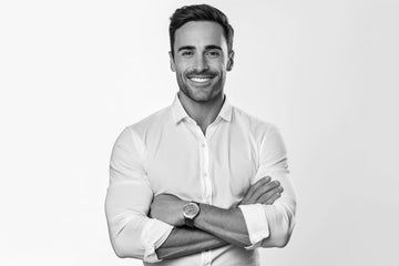 Confident man sporting stubble in a white shirt with crossed arms, embodying the modern debate of clean shaven vs stubble styles in men's grooming.