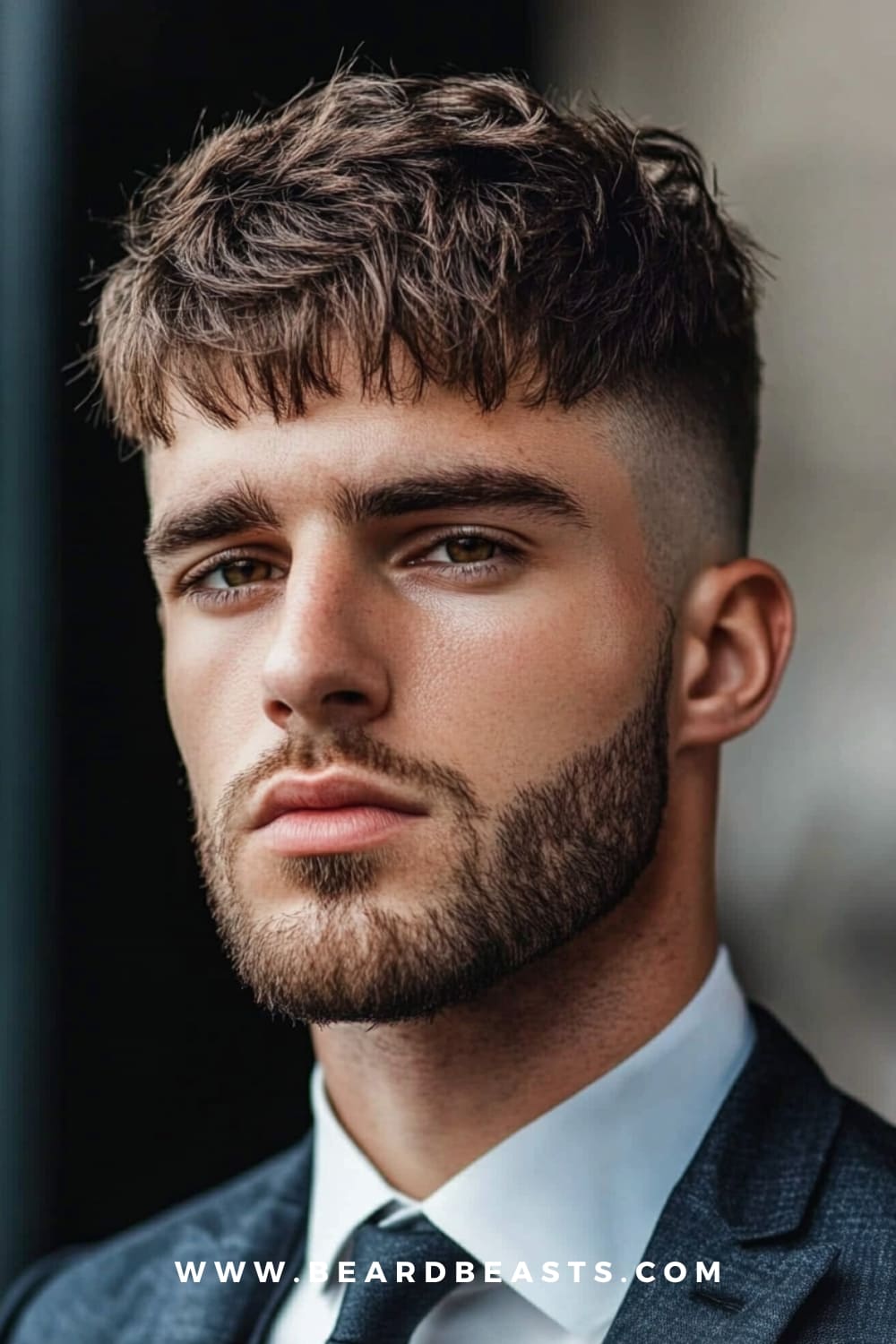 A man with a modern French crop haircut featuring textured, tousled hair on top and a short fade on the sides. Paired with a well-defined beard, this stylish haircut for men gives off a sharp, trendy look.