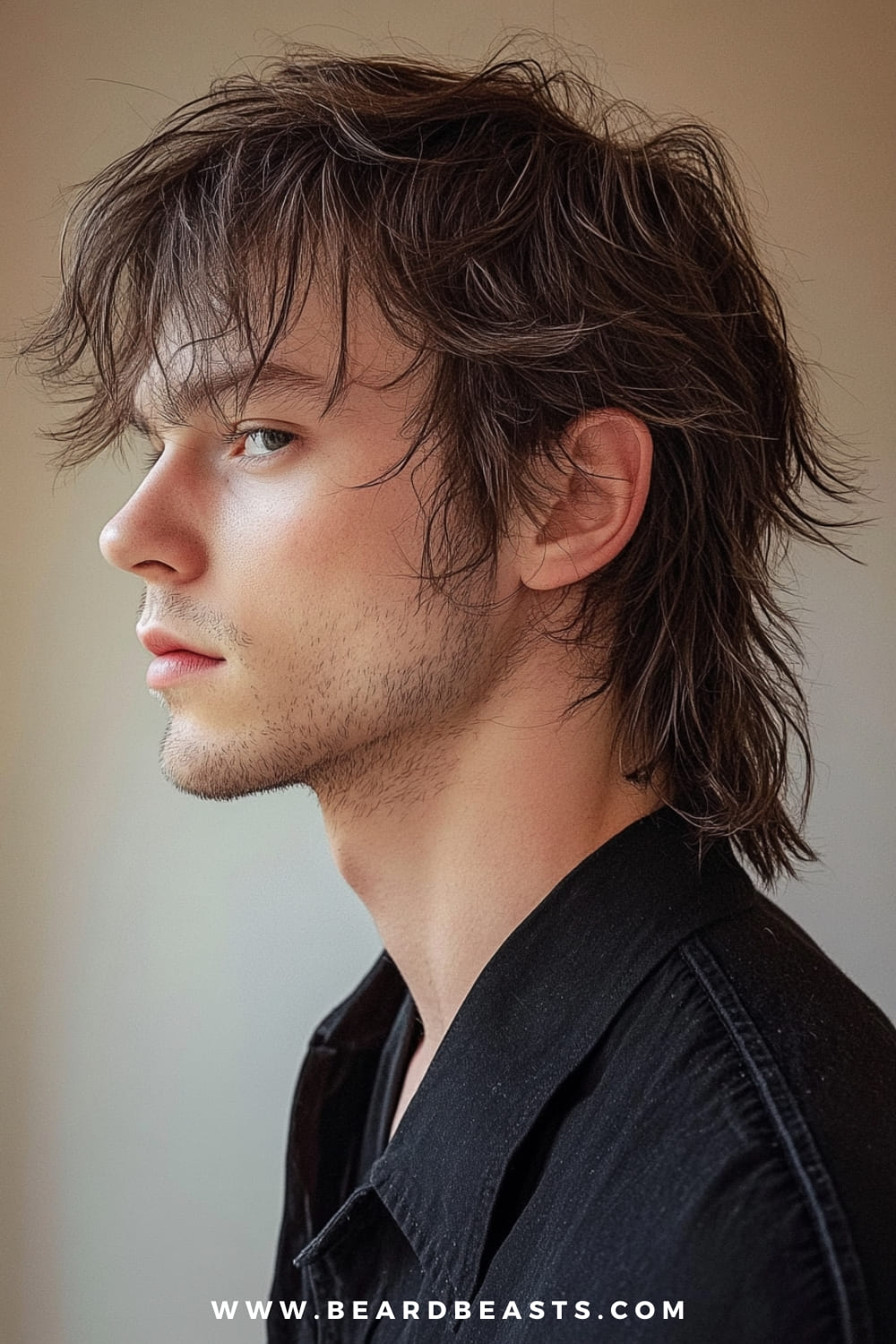 The image features a side profile of a young man with a slightly tousled, medium-length hairstyle. His hair has a natural, relaxed flow, with subtle layers that add movement and texture. The ends of his hair gently taper down, giving it a casual, unstructured appearance. He has a light stubble that adds to the laid-back, effortlessly cool vibe of his overall look. The soft lighting highlights the texture and depth of his hair, while the neutral background keeps the focus on his profile and hairstyle. The overall impression is one of understated style and easygoing charm.