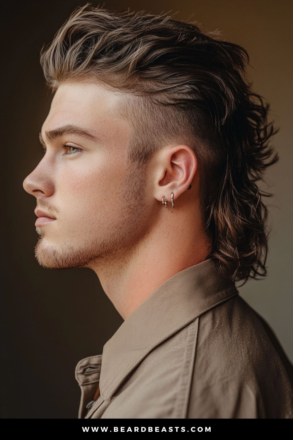 A side profile of a young man showcasing a bold modern mullet haircut. The style features short, sleek sides with a gradual fade that contrasts with the longer, wavy layers at the back. His hair is styled upward and backward on top, creating a voluminous, textured look that emphasizes the mullet’s signature flow. The man’s look is further complemented by silver hoop earrings and a khaki button-up shirt, giving him an edgy yet refined appearance that balances both retro and contemporary vibes.