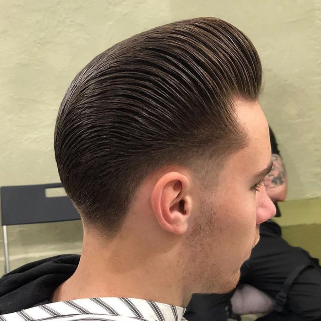 A side profile of a man sporting a sleek pompadour hairstyle, ideal for guys with smaller head shapes. The hair is combed back smoothly with added volume on top, giving the appearance of a fuller and more elongated head shape. The sides are tapered and neatly blended to enhance the contrast with the voluminous top. This classic pompadour is a great haircut choice for men with smaller heads looking to create a refined, stylish, and balanced look.