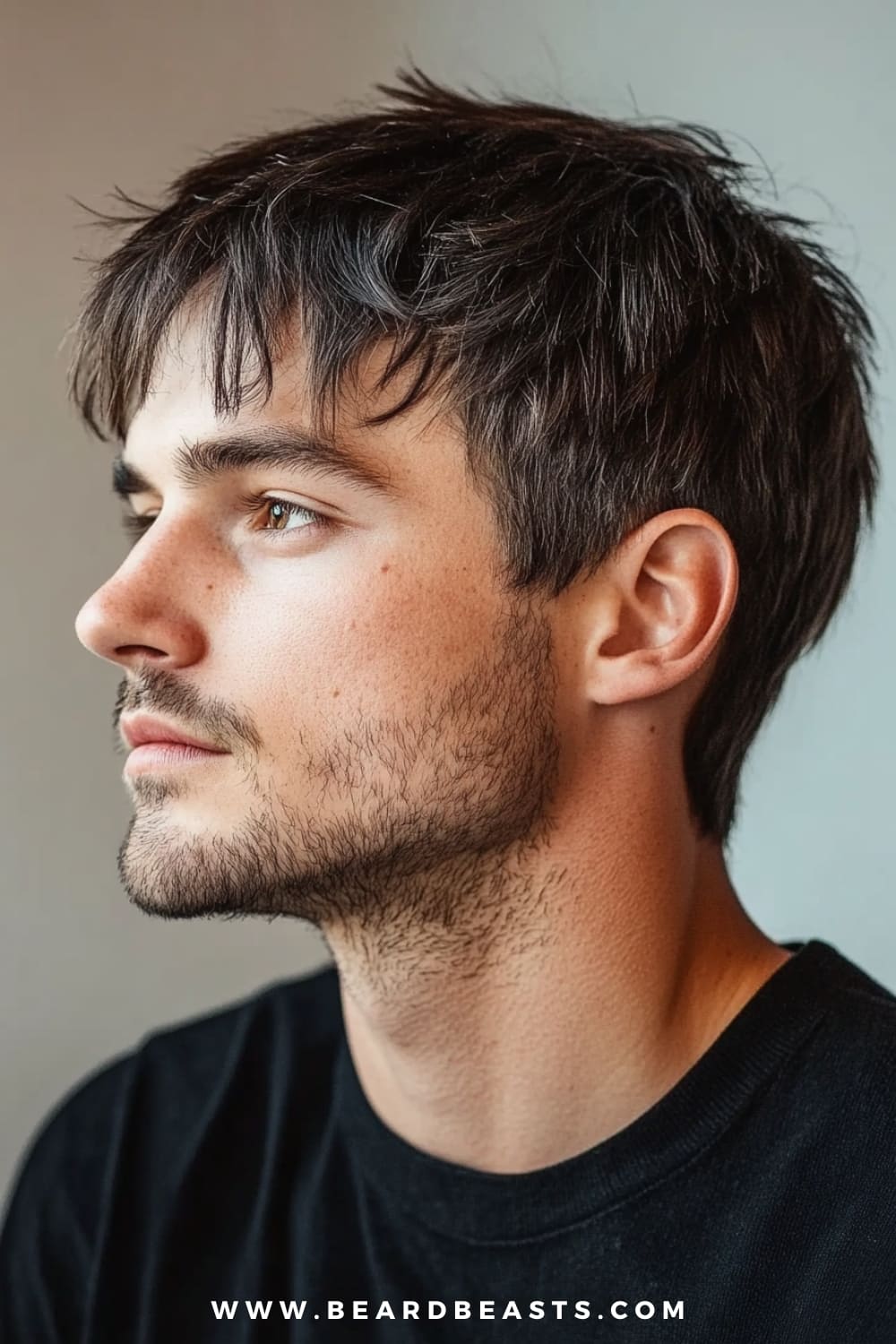 The image features a close-up side profile of a young man with a short shaggy hairstyle. His hair is slightly tousled, with subtle layers that add texture and movement while maintaining a neat, well-groomed appearance. The length is short, just enough to create a bit of volume on top, with the sides blending smoothly into the overall look. He has a light stubble that complements the casual, effortless style of his haircut. The lighting softly highlights the natural texture of his hair, while the neutral background keeps the focus on his profile and hairstyle. The overall vibe is clean, modern, and understated, perfect for those seeking a low-maintenance yet stylish look.