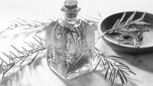 Vintage glass bottle with fresh rosemary sprigs inside, next to a wooden bowl of rosemary leaves, symbolizing natural Rosemary Oil for Beard Growth.