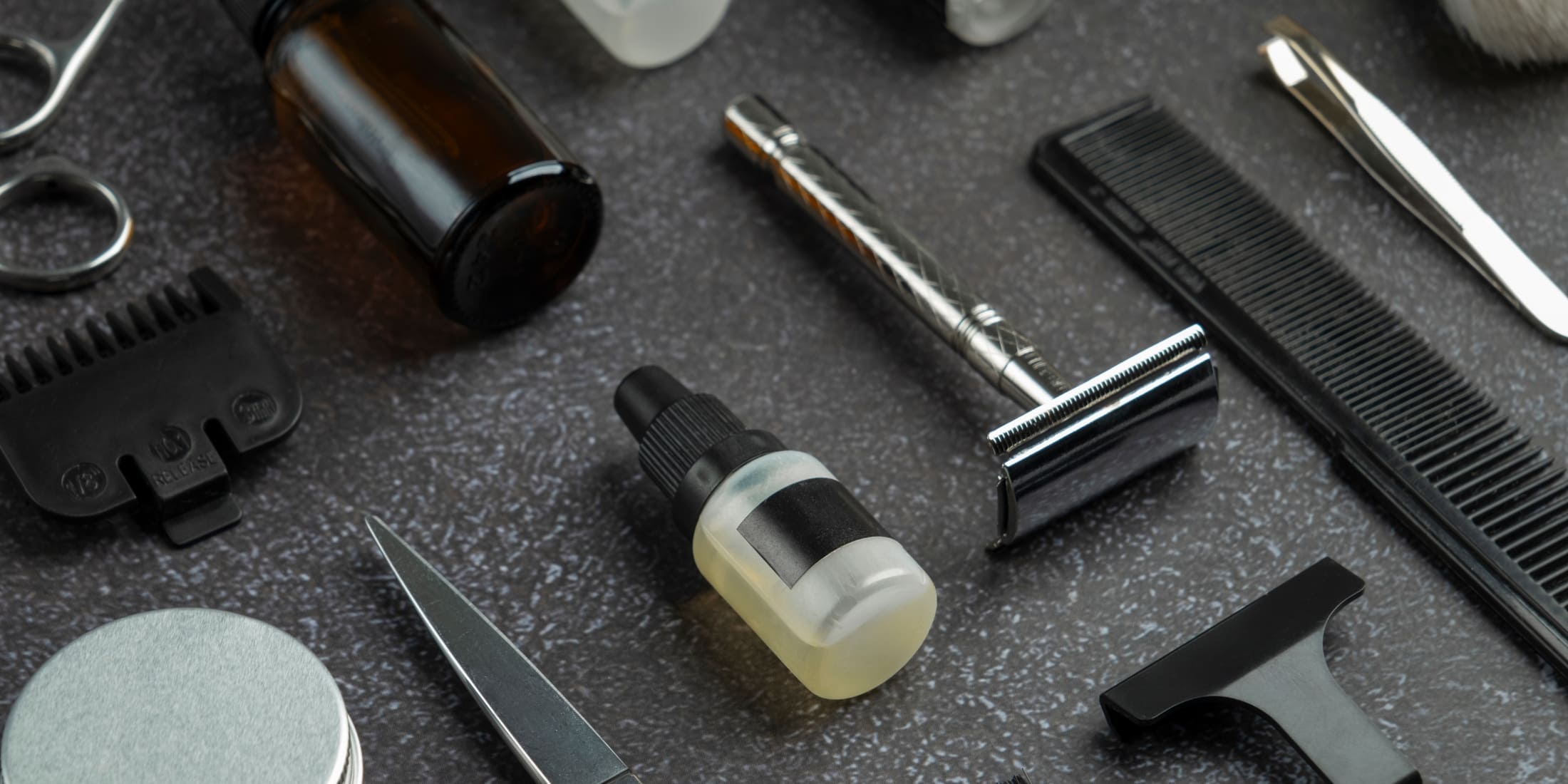 Close-up of various grooming tools including a safety razor, comb, scissors, and a small bottle of shaving oil, showcasing essential shaving accessories for the ultimate shave in the straight razor vs safety razor debate.