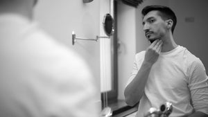 Man examining his see-through beard in the mirror, considering care tips for a fuller look