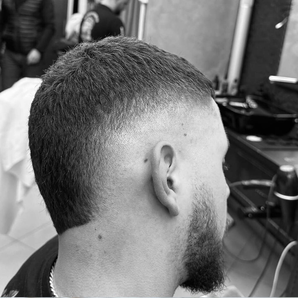 Black and white side view of a well-groomed haircut transitioning from shorter sides to a slightly longer, even top. The hairstyle is neat and clean, with sharp edges and a structured neckline. Paired with a trimmed beard, it creates a polished and modern appearance. Perfect for those who prefer a simple, low-maintenance look.