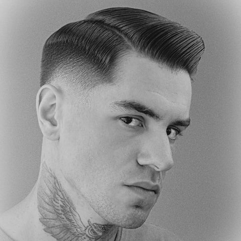 Man with a sleek Side Part haircut, featuring a precisely defined part and smooth, combed back hair. The sides are expertly tapered into a clean fade, creating a polished and classic look.