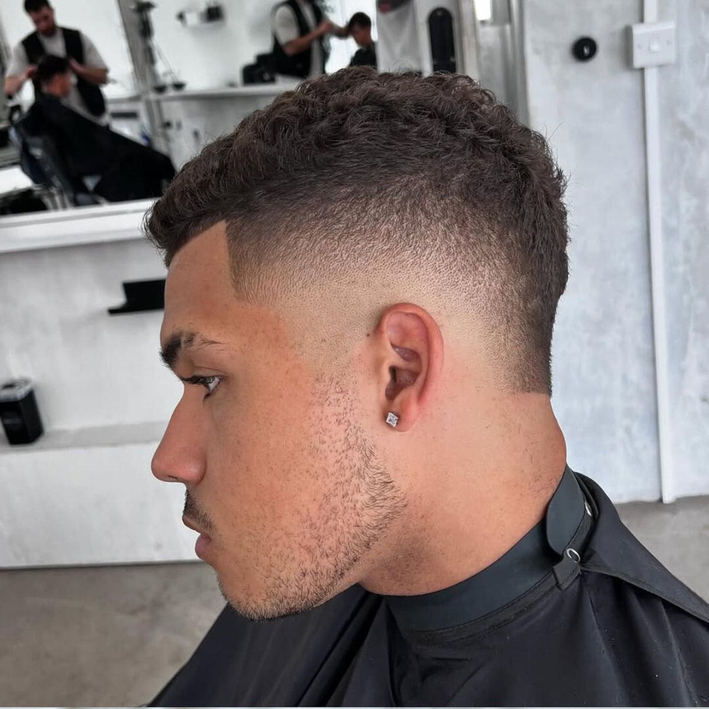 Side view of a clean and stylish Skin Burst Fade haircut with short curly hair on top. The fade transitions smoothly from the skin at the bottom to fuller hair near the crown, creating a sharp, modern look. Perfect for showcasing facial features and low-maintenance styling. A trendy Short Hair Burst Fade ideal for men with textured or curly hair.