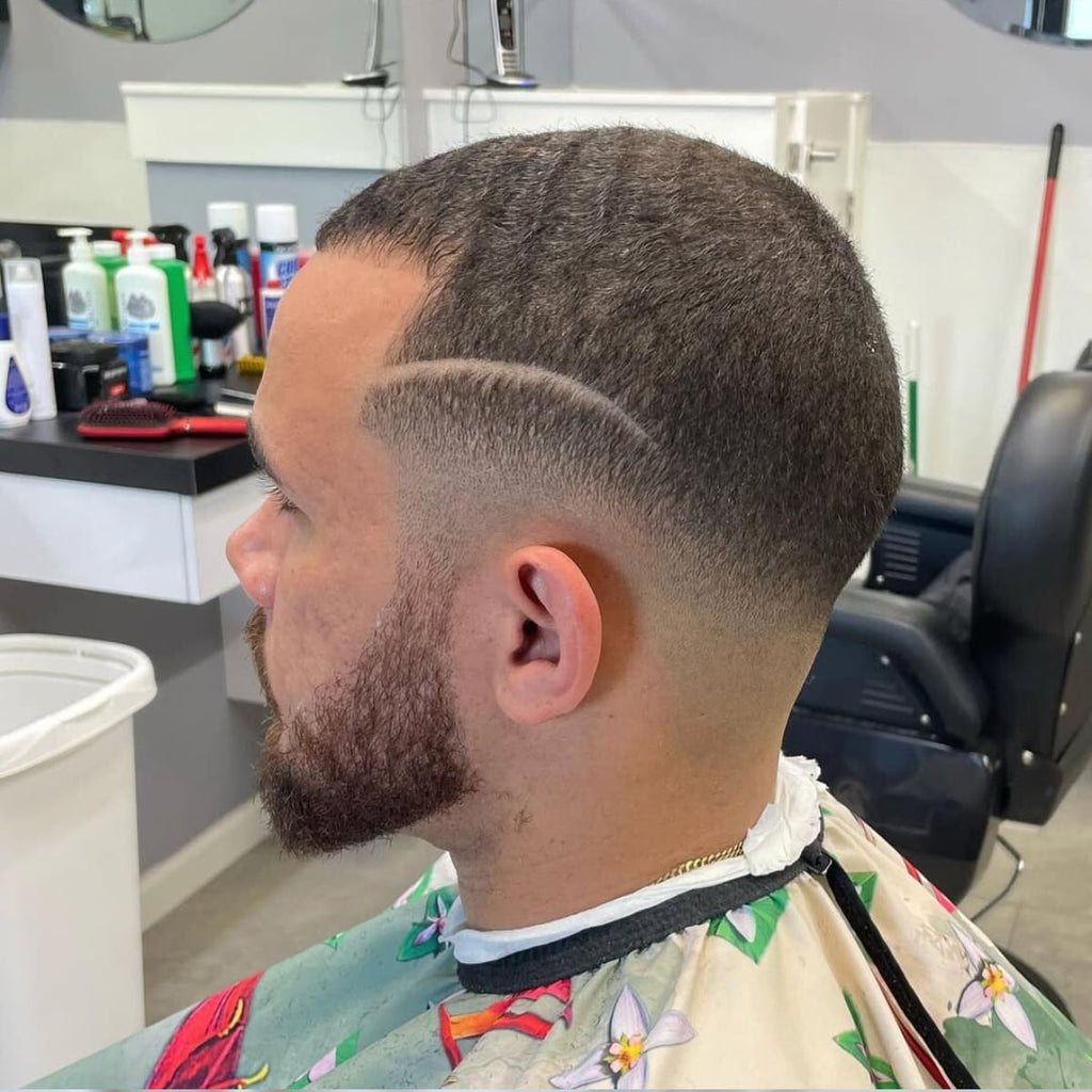 A side profile of a man with a clean haircut featuring a sharp blend transitioning smoothly from the scalp to short hair on top. The style includes a unique curved design shaved into the side, adding a creative and modern touch.