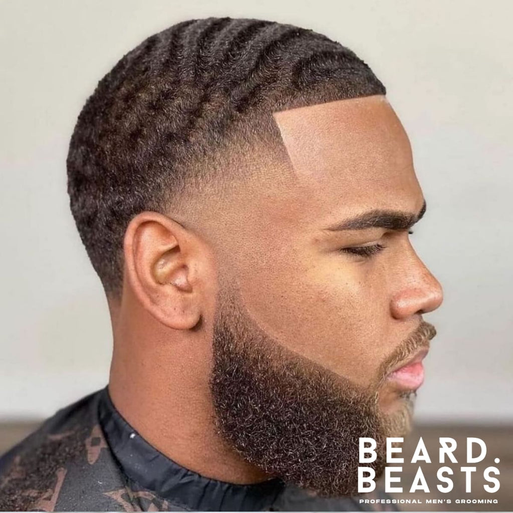 A close-up side view of a man with neatly styled short hair featuring defined waves, a sharp blend around the sides, and a perfectly groomed beard. The haircut and beard blend seamlessly, creating a polished and modern look.