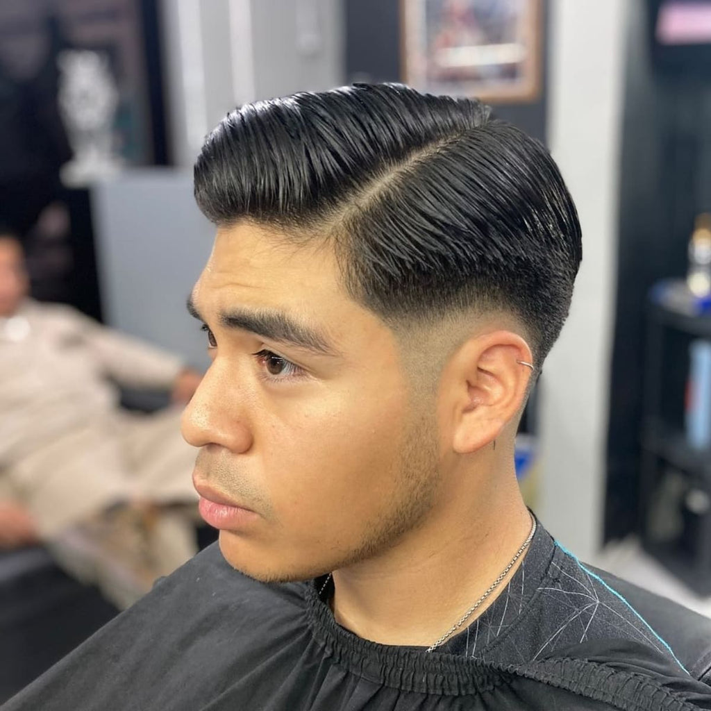 A side profile of a man with a sleek, neatly combed hairstyle featuring a sharp side part. The fade transitions smoothly from longer hair on top to a close, tapered cut around the ears. The overall look is clean, polished, and well-groomed, showcasing a timeless and refined haircut.