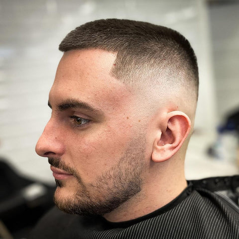 Close-up of a man with a buzz cut hairstyle, featuring a tight fade that blends seamlessly into the skin. This classic hairstyle for men is the epitome of simplicity and practicality, offering a clean, low-maintenance look that’s perfect for any occasion.