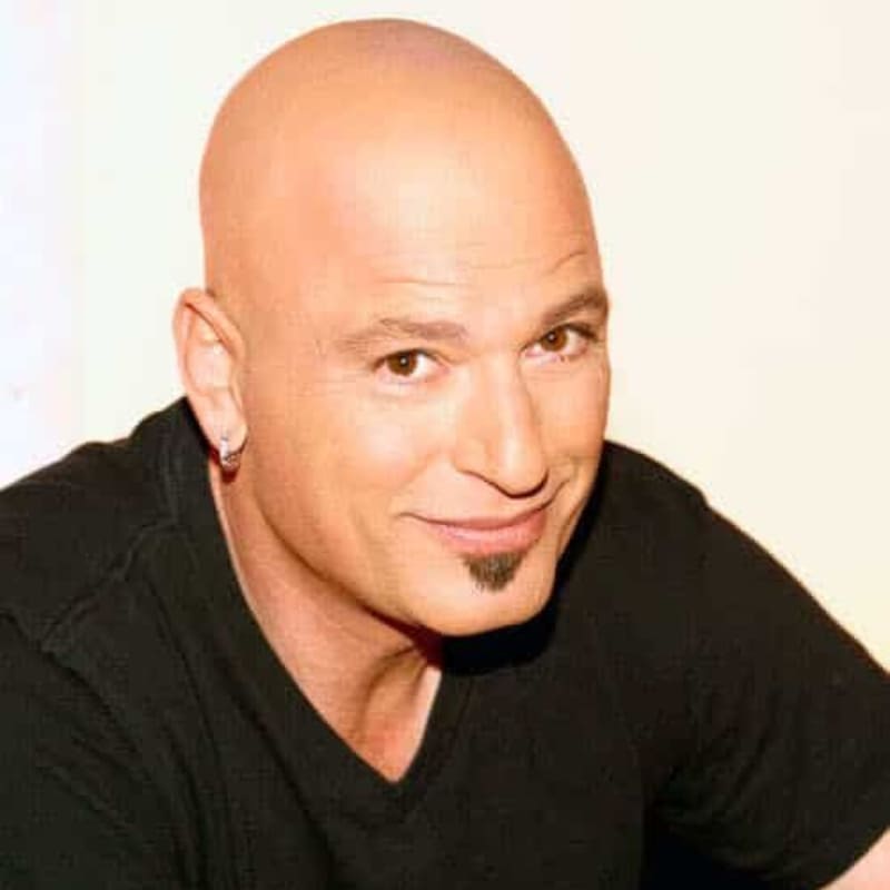 Bald man with a soul patch and earring, smiling in a black shirt