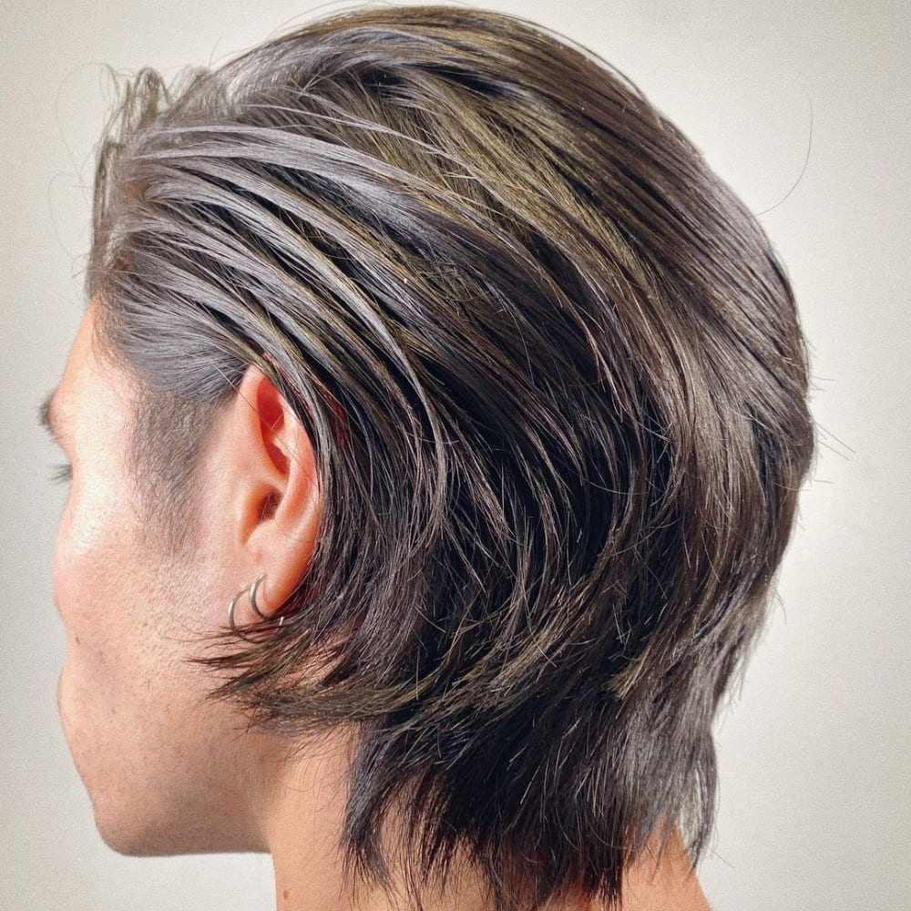 Man with straight hair styled in a long layered haircut, featuring smooth, flowing layers that add texture and movement. He is wearing a small hoop earring and looking to the side, showcasing the natural shine and volume of his hair in a well-lit setting.