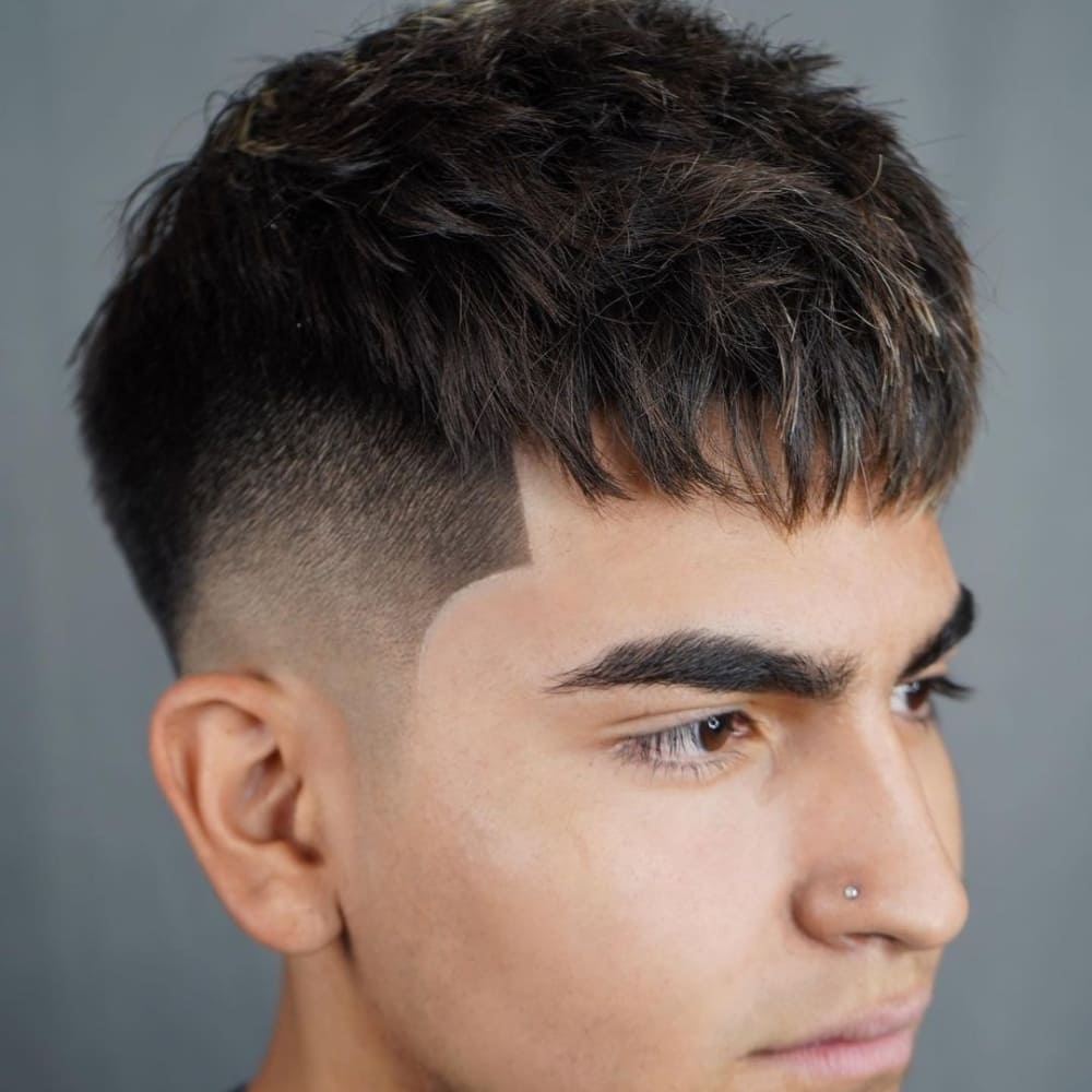 Young man with straight hair styled in a textured crop haircut, featuring short sides with a high fade and a longer, tousled top. He has a neatly groomed line-up along the forehead and a small nose piercing, giving him a modern, edgy look.