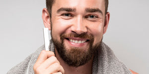 Smiling man holding a straight razor, highlighting the benefits and experience of using a straight razor in the straight razor vs safety razor comparison.