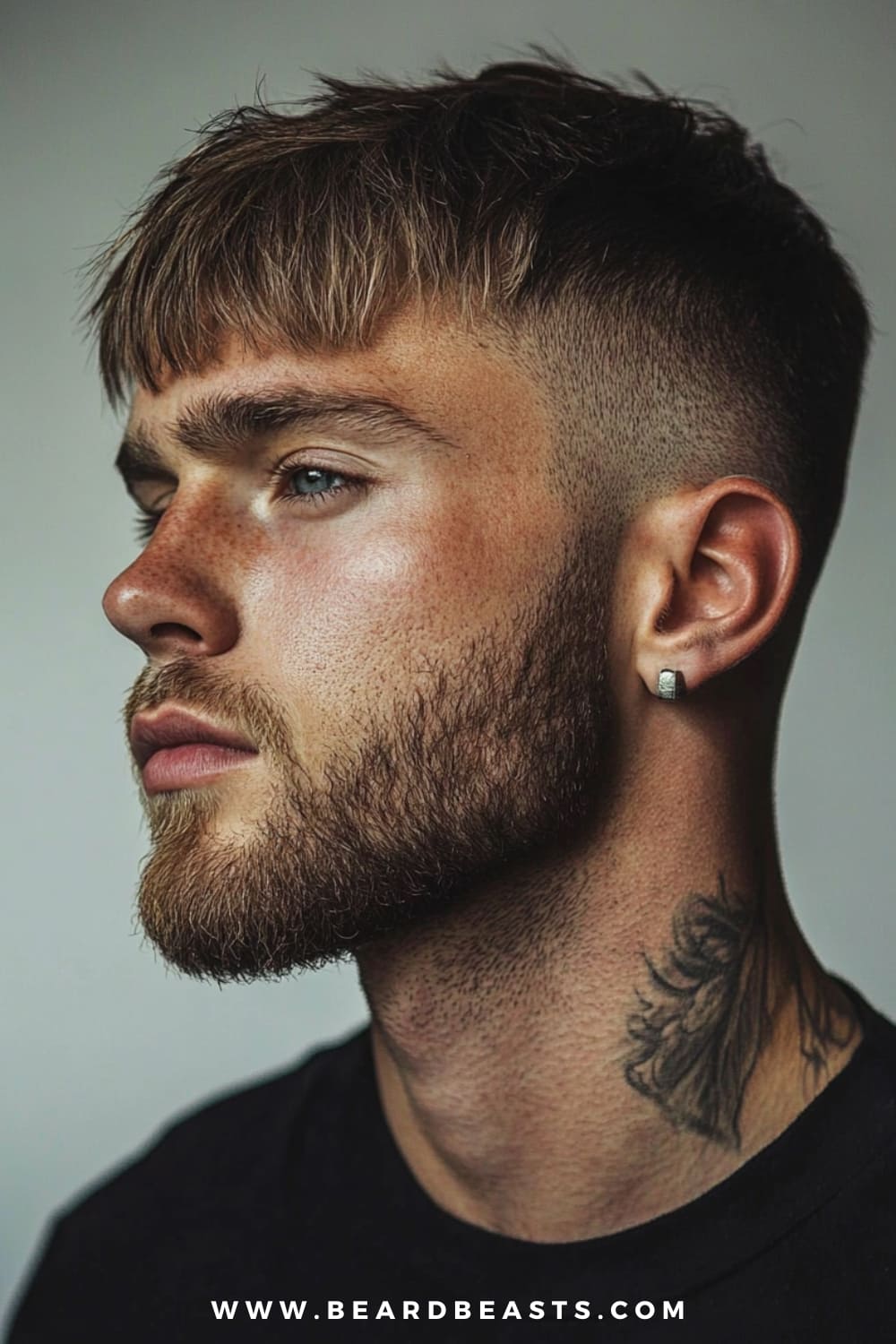 A man confidently sports a textured crop, a trendy choice among hairstyles for men with thick straight hair. His thick, straight hair is cut into choppy layers on top, creating a textured and tousled look, while the sides are neatly faded for a clean, sharp contrast. He has a well-groomed beard and wears a small earring, adding a touch of personal style. A subtle neck tattoo peeks out from his black shirt, enhancing his edgy yet polished appearance.