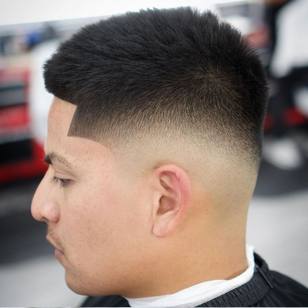 Side profile of a man with a sharp and modern haircut. The style features a precise lineup at the hairline, transitioning seamlessly from the textured top into a clean and smooth taper around the sides and back. The hair on top is slightly longer, styled naturally to maintain volume and texture. A sleek and polished look perfect for a fresh and versatile appearance.