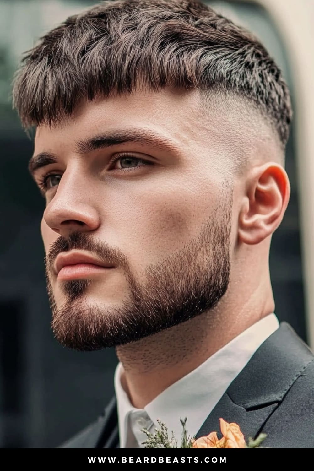 A groom with a modern French Crop hairstyle, showcasing one of the top men's wedding hairstyles. His hair is neatly cropped with a textured fringe, and the sides are expertly faded, creating a clean and sharp look. The well-groomed beard complements the hairstyle, adding to the overall refined and sophisticated appearance. Dressed in a classic black suit with a white shirt, and adorned with a boutonniere, he exudes confidence and style, making this hairstyle an excellent choice for a contemporary wedding setting.