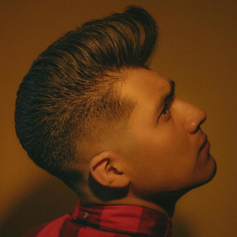 Profile of a man with a classic pompadour hairstyle, showcasing voluminous, swept-back hair with a clean fade. This timeless look captures the essence of vintage style with a modern twist, making it a perfect choice for men seeking a bold and polished appearance.