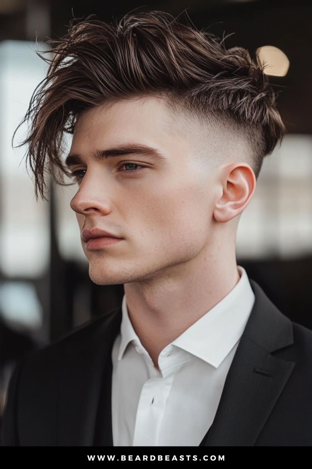 A groom with a trendy Undercut hairstyle, showcasing one of the most popular men's wedding hairstyles. His hair is styled with significant volume and texture on top, contrasted by the sharply faded sides, creating a bold and modern look. The hairstyle complements his clean-shaven face and sharp jawline, adding to the overall sleek and sophisticated appearance. Dressed in a tailored black suit and white shirt, he exudes confidence and contemporary elegance, making this hairstyle an excellent choice for a stylish wedding day.