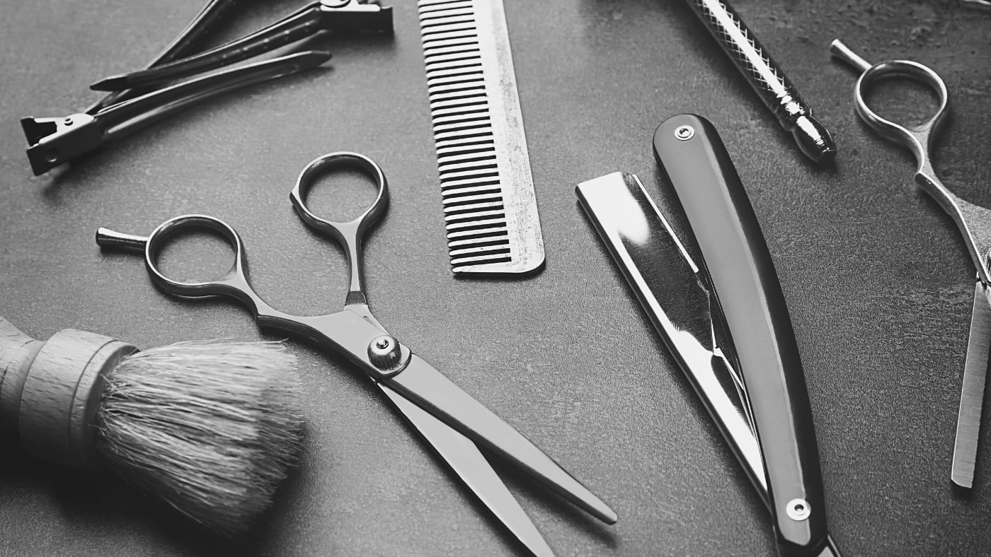 Barber's toolkit with sharp scissors, comb, straight razor, and shaving brush on a grey background, essential for styling a number 5 buzz cut.