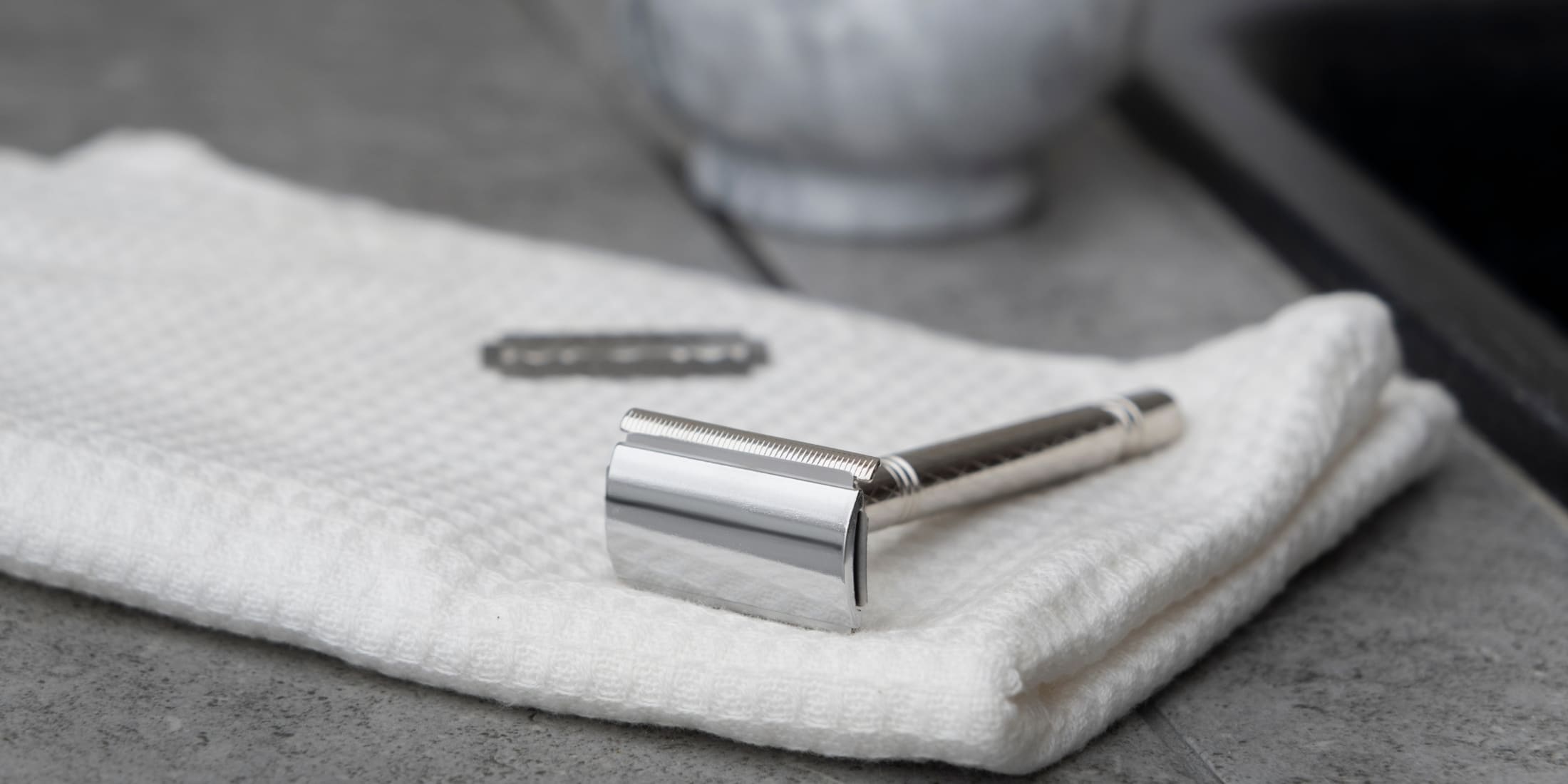 Stainless steel safety razor resting on a folded white towel with a replacement blade nearby on a bathroom countertop, illustrating the classic design and precision of safety razors. Perfect for discussions on safety razor vs cartridge razor comparisons.