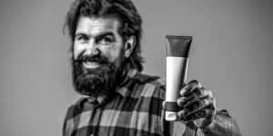 Man with a full beard smiling and holding a tube of beard conditioner, demonstrating what beard conditioner is and how to use it for soft, healthy beard care.