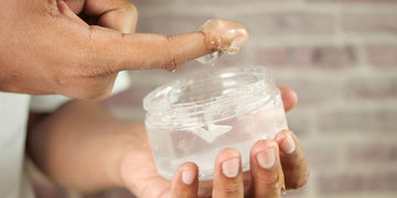 A close-up image of a person demonstrating how to use hair gel by dipping their finger into a jar of clear hair gel.