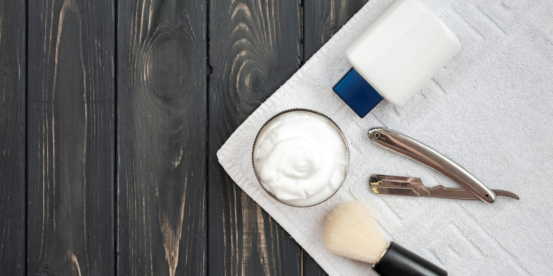 Shaving kit with post-shave balm, straight razor, brush, and towel on a dark wooden background, highlighting what is post-shave balm used for