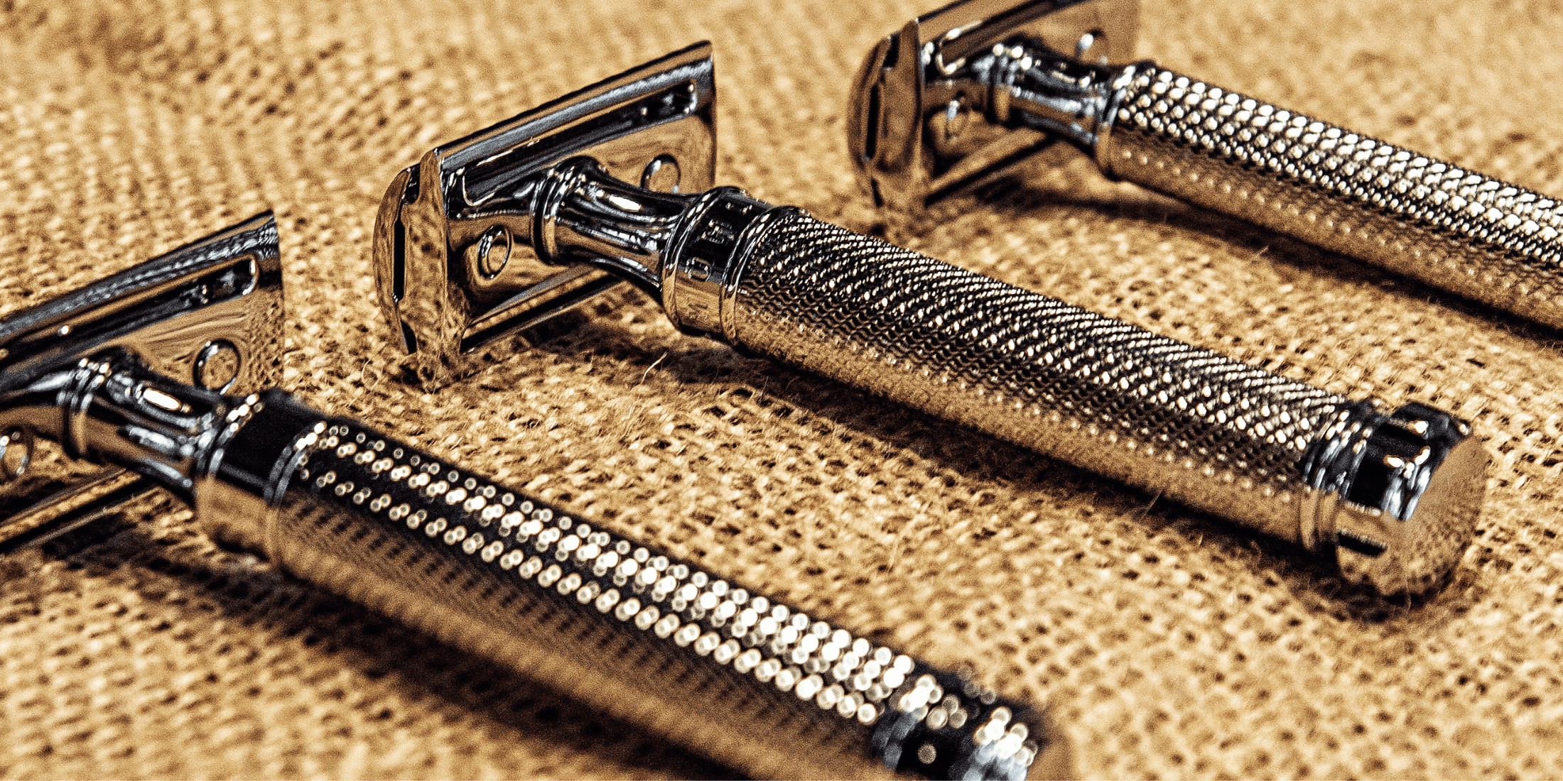 Three shiny safety razors with textured handles are laid out on a burlap surface. This image prompts the question: how often should you change your razor blades?