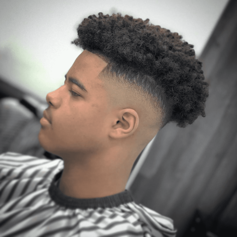 ide profile of a young man with an Afro Fade haircut, featuring a voluminous, curly afro on top with a clean fade on the sides and back. This hairstyle blends the natural texture of an afro with the modern appeal of a fade, making it a trendy choice for men seeking fashionable fade haircuts