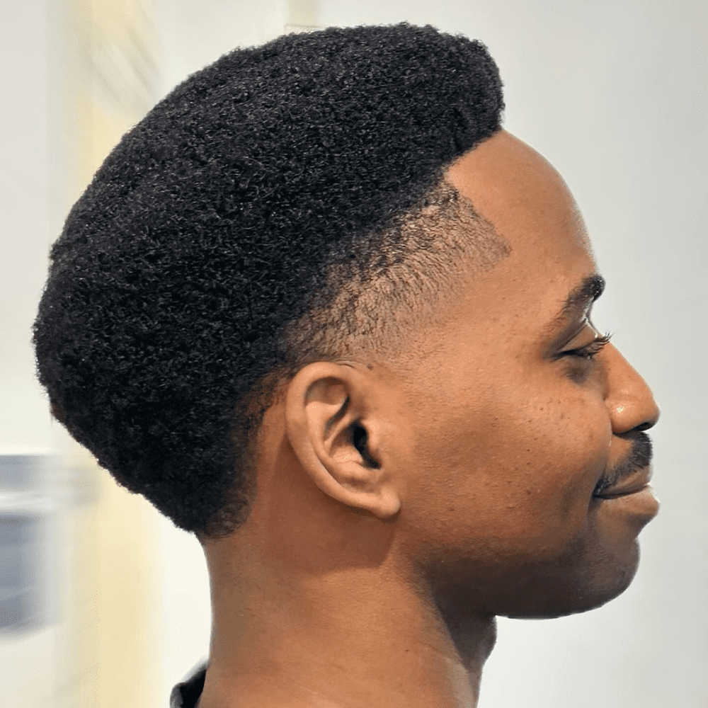 Side profile of a man with an Afro Temple Taper Fade haircut, showcasing a natural afro texture with a taper fade around the temples. The hairstyle highlights a fresh, modern look, perfect for men who want to combine traditional afro styles with trendy fade haircuts