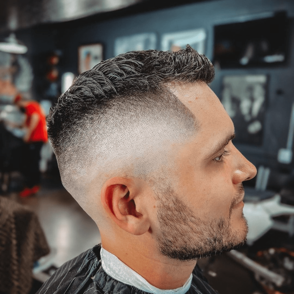 Man with a short fade haircut featuring a bald fade and textured top. The hairstyle showcases a clean bald fade on the sides and back, blending seamlessly into the textured, styled hair on top. This modern and sharp look is ideal for men's hairstyles in 2024, offering a stylish and edgy appearance