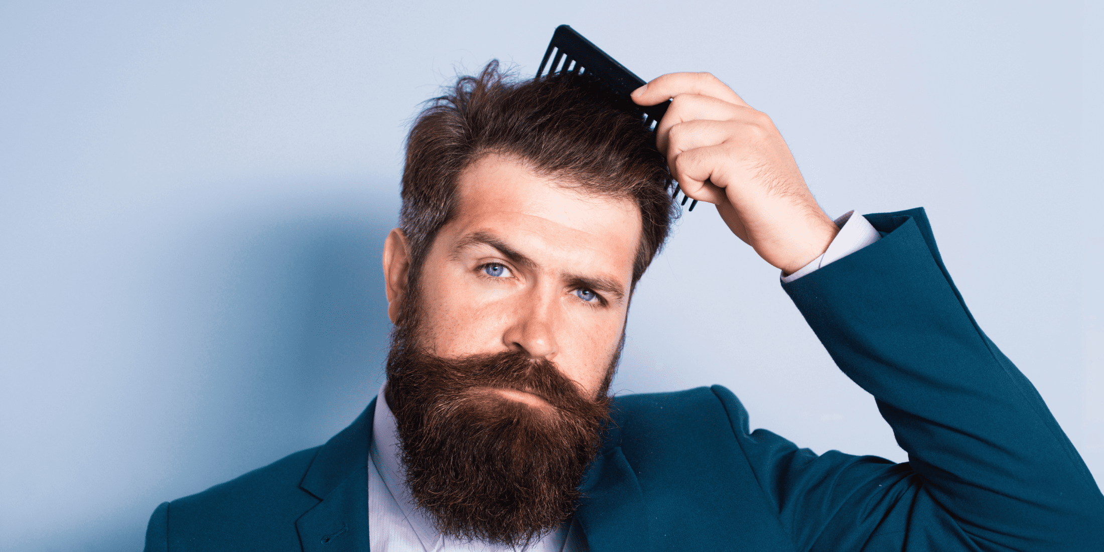 Bearded man in a blue suit brushing his styled hair, demonstrating what hair clay can do for a well-groomed look. The image shows how to use hair clay to achieve a strong hold and natural finish, highlighting what does hair clay do to add volume and texture to various hair types.