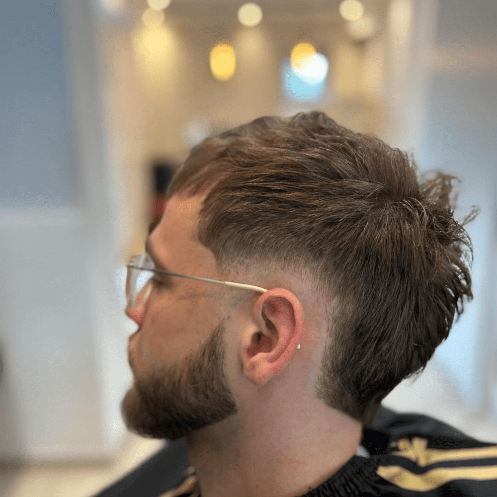 Side profile of a young man with a Burst Fade haircut, featuring textured hair on top and a unique semi-circular fade around the ears. The hairstyle provides a modern and edgy look, making it a trendy choice for men seeking stylish fade haircuts