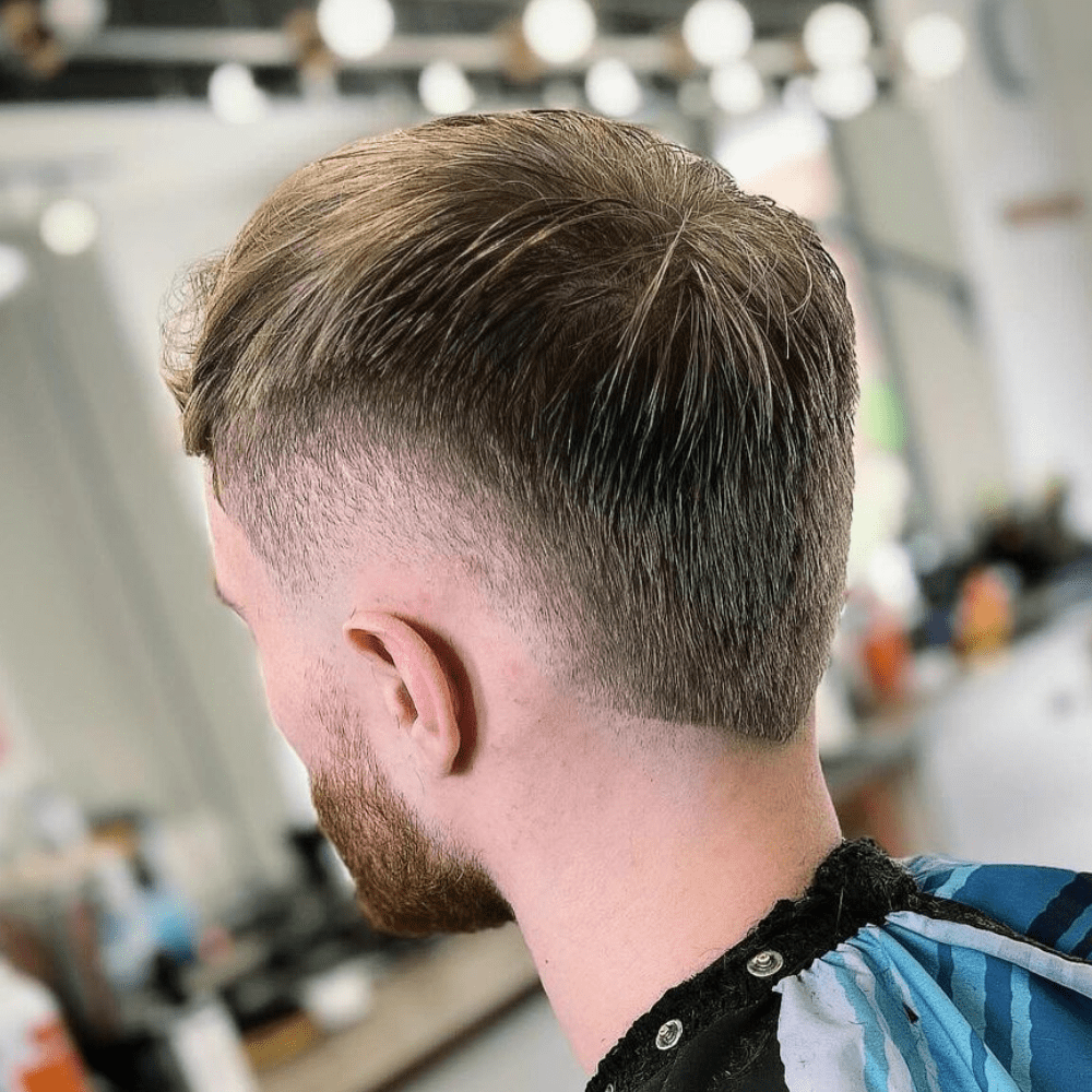 Side profile of a man with a Burst Fade haircut, featuring straight hair on top that smoothly transitions into a fade down the sides and back. The hair is neatly combed, enhancing the clean and structured appearance. The fade begins just above the ears and tapers down, providing a modern and polished look. The setting is a contemporary barbershop with a blurred background, emphasizing the precision and sharpness of the haircut. This burst fade is ideal for men with straight hair who seek a stylish and sophisticated hairstyle.