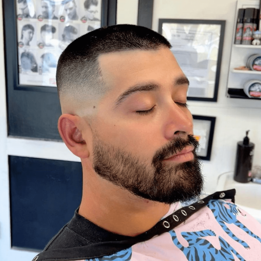 Man with a short buzz cut fade haircut. The hairstyle features a very short buzz cut on top with a clean, gradual fade on the sides and back. This low-maintenance, stylish look is perfect for modern men's short fade haircuts in 2024, offering a sharp and polished appearance.