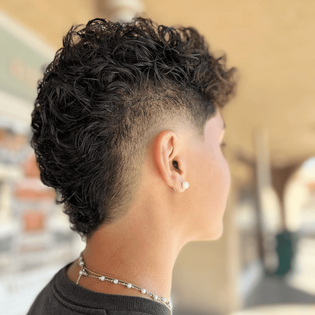 Side profile of a classic burst fade mohawk haircut featuring voluminous, curly hair on top and a clean fade around the ears. The fade gradually blends into the textured curls, creating a bold yet stylish look ideal for individuals with wavy or curly hair.