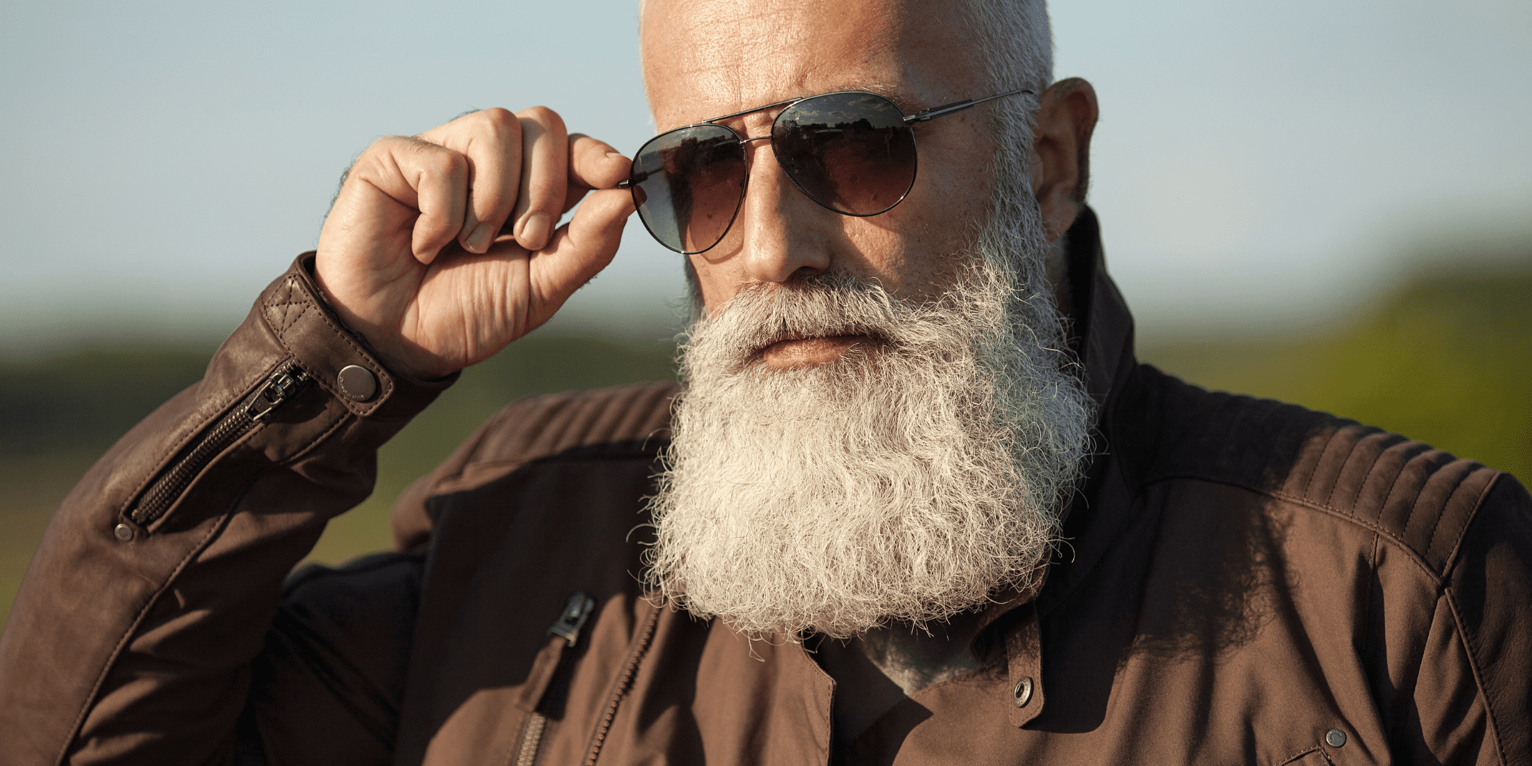 Older man with a full, white beard wearing sunglasses and a leather jacket, debunking the myth that beards make you look older. Highlighting how a well-groomed beard can enhance facial features and contribute to a stylish, distinguished appearance.