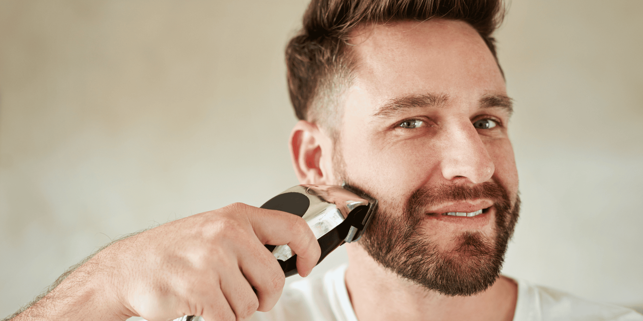 Smiling man trimming his beard with an electric trimmer, addressing the common myth that trimming reduces beard growth. Highlighting the importance of regular trimming for maintaining a healthy and well-groomed beard. Debunking myths about beard growth and effective beard care.